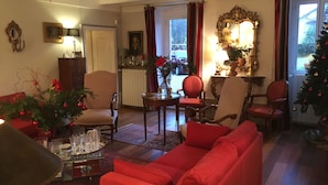 A cozy living room with a red sofa, a coffee table, and a fireplace. There are two chairs, a side table, and a Christmas tree.