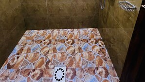 Eine Dusche mit Duschbrause, kleinem Fenster und Ablauf.