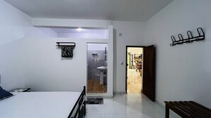 Ein Schlafzimmer mit Bett, Nachttisch, einer Bank, einem Badezimmer mit Waschbecken und einer Tür zu einem anderen Raum.
