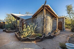 Un edificio con un exterior perforado único, un jardín de cactus y una pequeña entrada en arco.