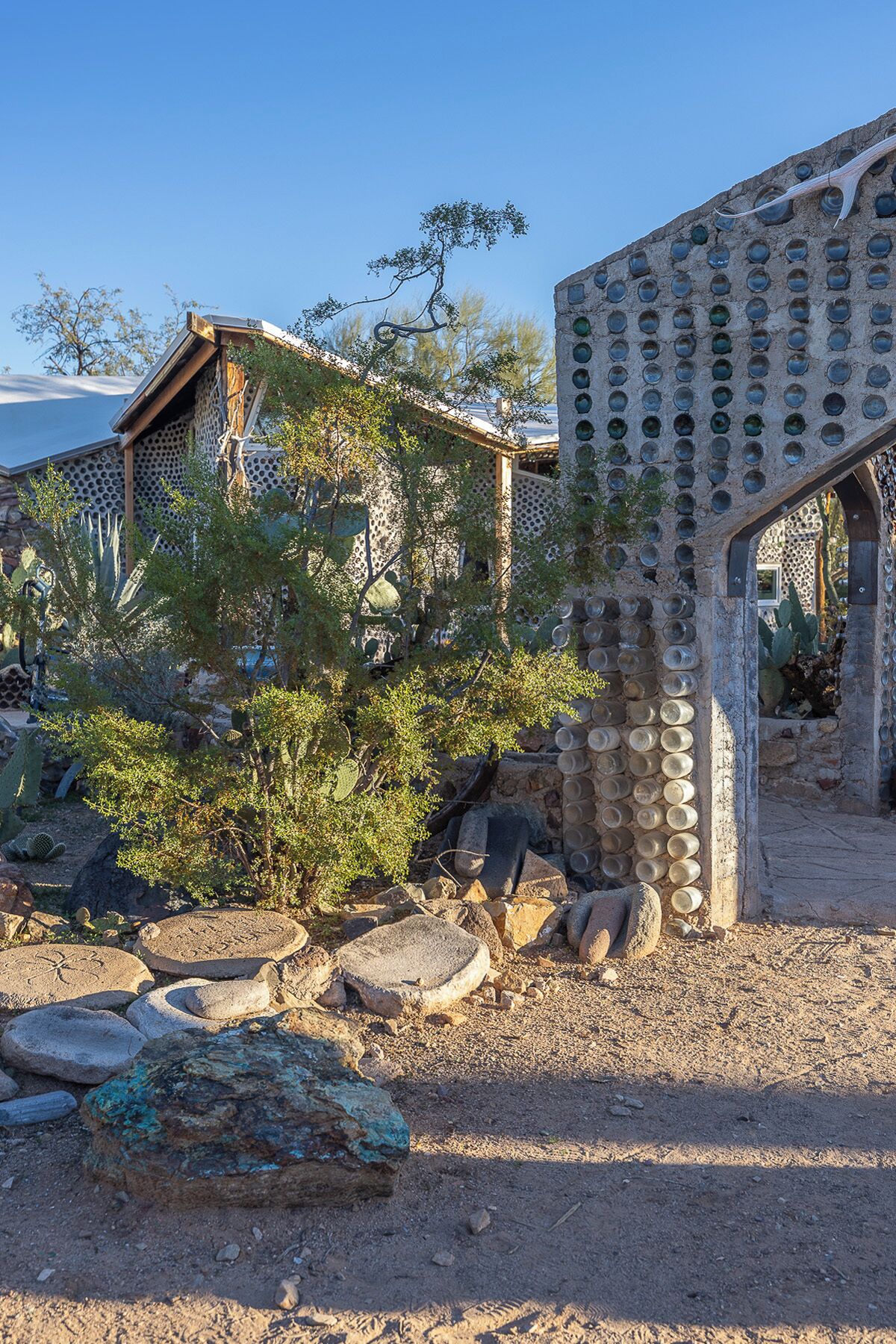 Un edificio rústico con un diseño circular único en sus ventanas, rodeado de vegetación y rocas propias del desierto.