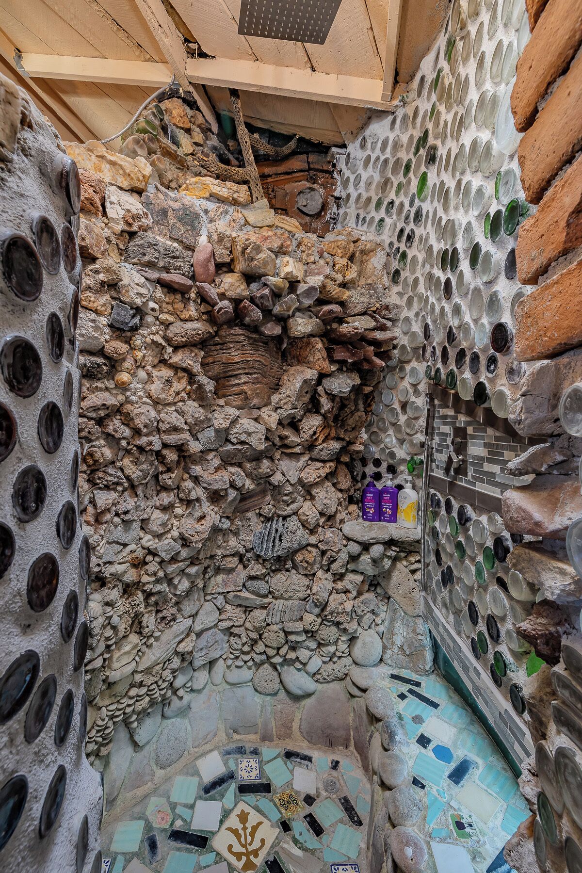 A stone-walled room with a tiled floor, a wooden ceiling, and a metal grate.