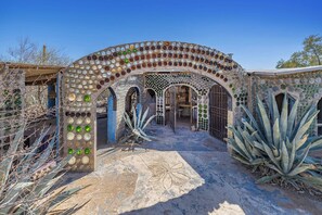 Un bâtiment doté d’une arche ornée de mosaïques, d’un aménagement paysager aride et surplombant un ciel dégagé.