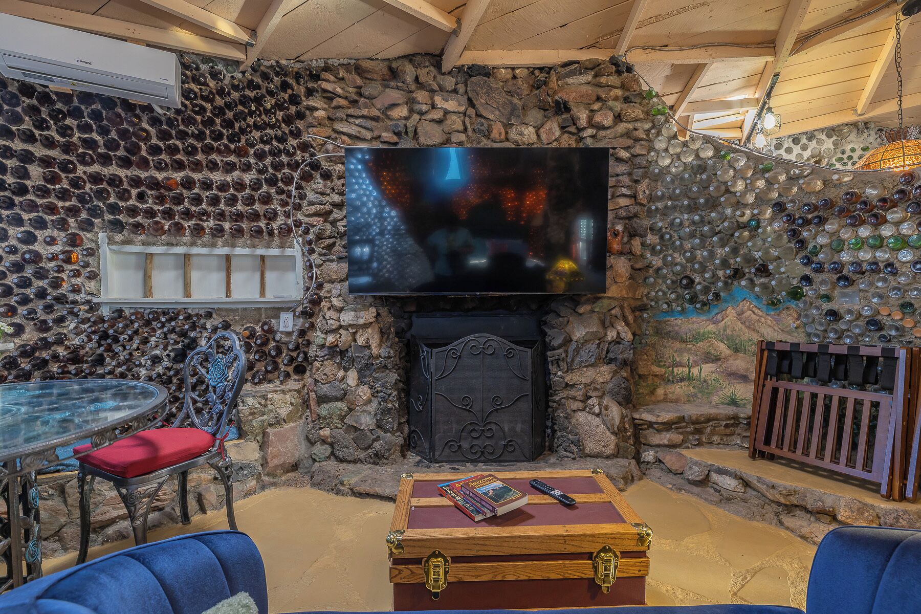 Une pièce aux murs de pierre, dotée d’une cheminée, d’un téléviseur et d’une table sur laquelle est posé un coussin rouge.