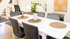 Ein weißer Esstisch mit vier Stühlen, eine Vase mit weißen Blumen und gewebten Tischsets.