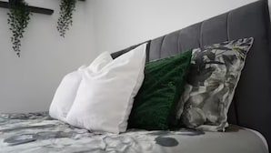 Ein Bett mit grauem Kopfteil, einem weißen, einem grünen und einem blumigen Kopfkissen.