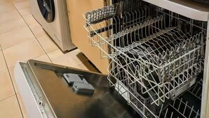 Eine Küche mit Waschmaschine, Spüle, Geschirrgestell und einem Fenster mit durchsichtigen Vorhängen.