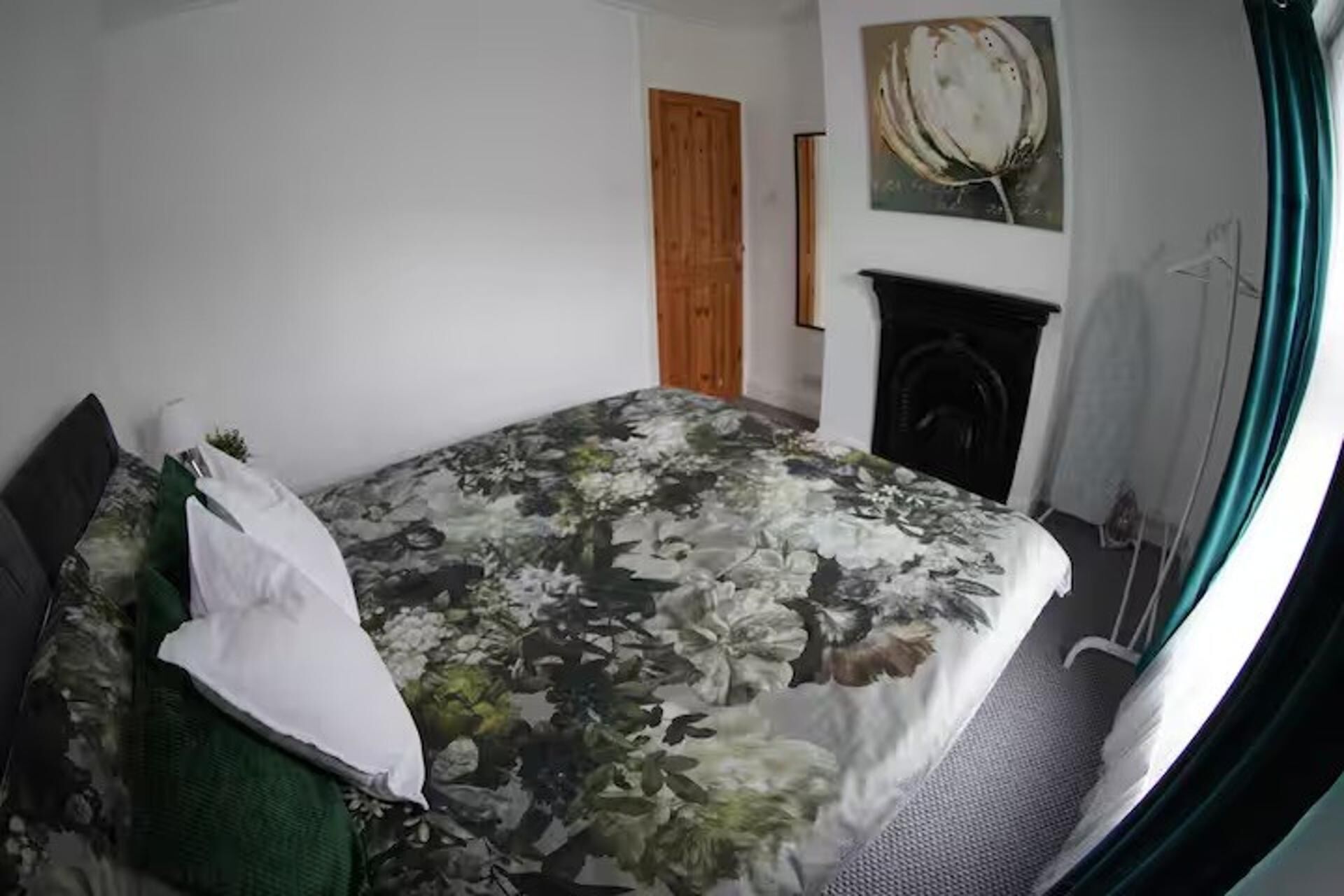 A bedroom with a bed, a wooden door, a fireplace, and a painting on the wall.