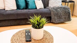 Ein Wohnzimmer mit einem dunklen Sofa, einem weißen Couchtisch, einer Fernbedienung und einer Topfpflanze.