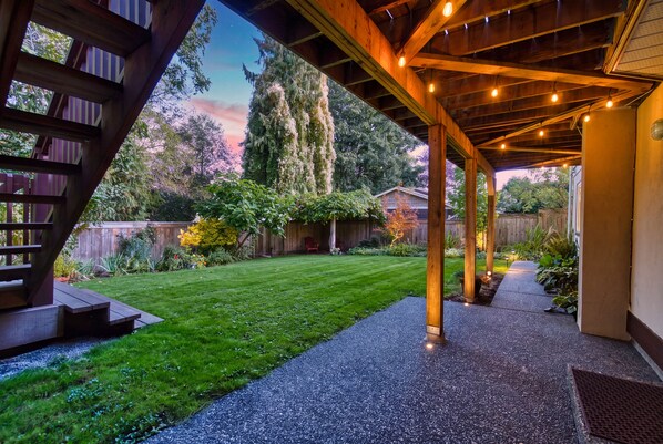 A covered outdoor area with a wooden deck, a gravel path, and a grassy lawn.