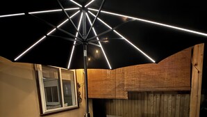 Un patio al aire libre con una mesa, sillas, una lámpara en el techo y una cerca de madera.