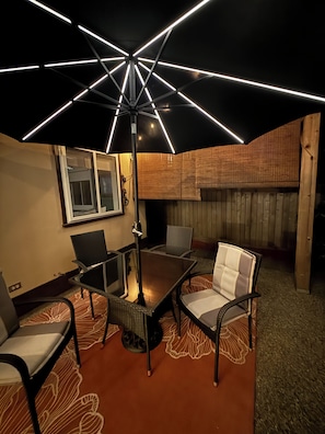 Une terrasse extérieure avec une table et des chaises, un luminaire suspendu au plafond et une clôture en bois.