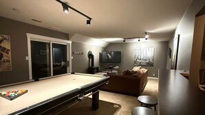 Una mesa de billar, una zona de bar y un área de estar con televisor en una habitación con paredes grises.