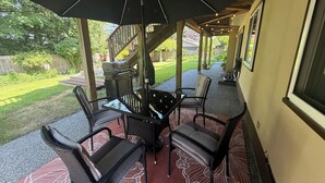 Un patio exterior con mesa y sillas, una parrilla y un área cubierta con vistas al jardín trasero.