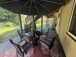 Une terrasse extérieure avec une table et des chaises, un barbecue et un espace couvert offrant une vue sur le jardin arrière.