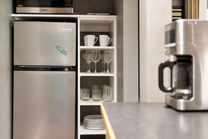 Una cocina con un refrigerador de acero inoxidable, una cafetera y estantes con tazas, vasos y platos.