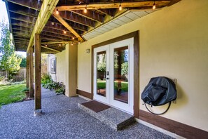 Un espacio al aire libre cubierto con techo de madera y luces colgantes, una puerta con paneles de vidrio y un bolso negro colgado en la pared.