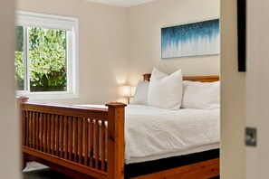 Un dormitorio con una cama de madera, una ventana con vistas a zonas verdes y un cuadro en la pared.