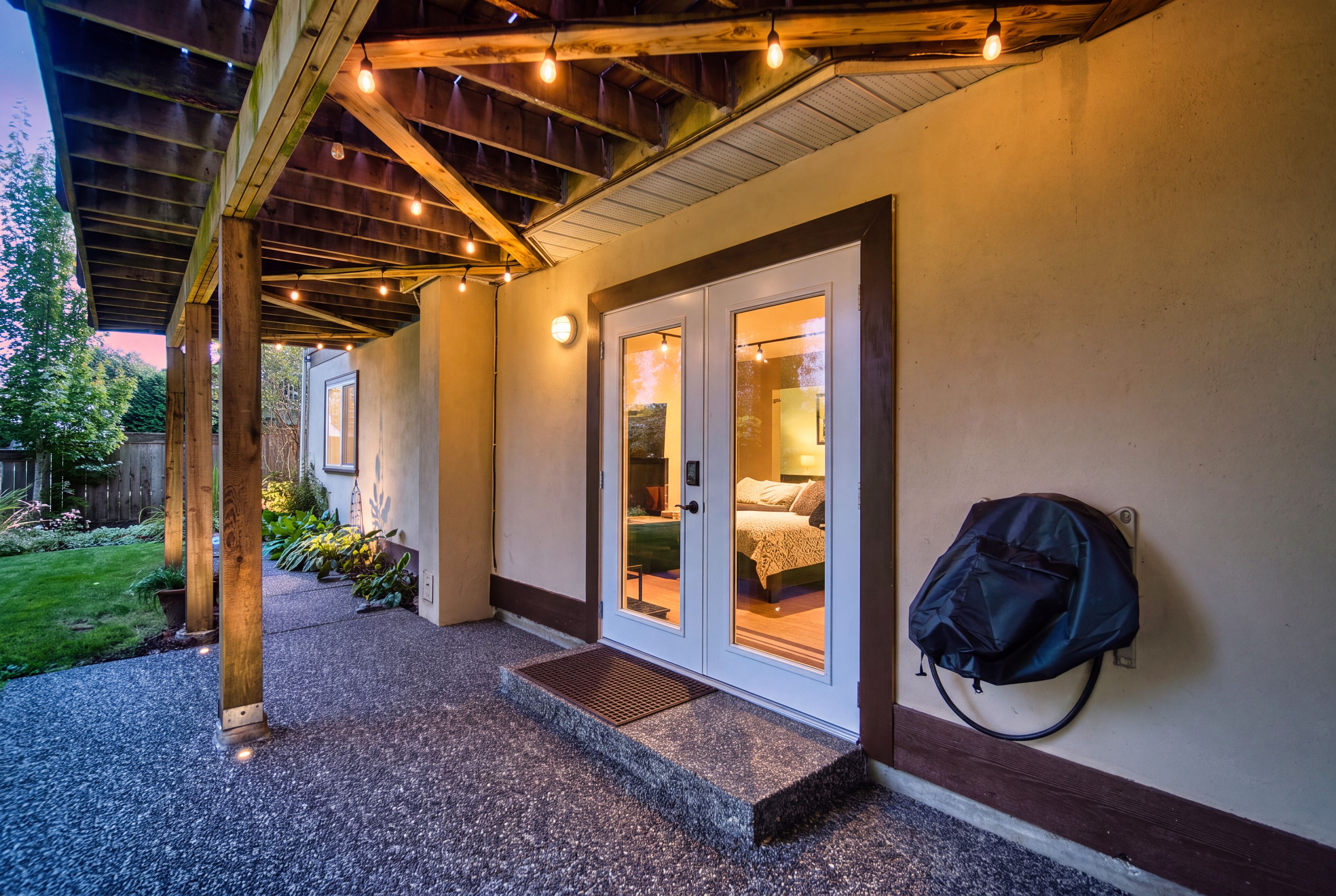 A covered outdoor area with a gravel path leading to a building with glass doors and a bed visible inside.