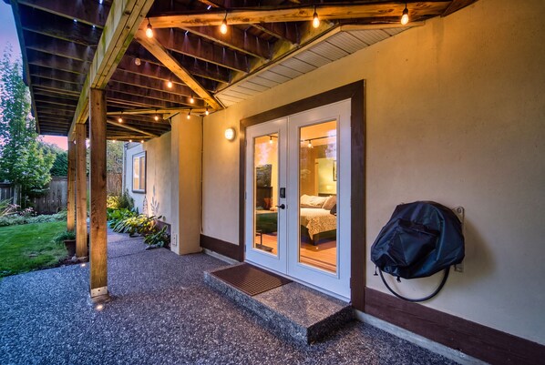 Un espacio al aire libre cubierto con un camino de grava que lleva a un edificio con puertas de vidrio y una cama visible en su interior.