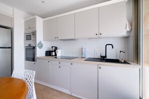 Eine moderne Küche mit weißen Schränken, einem Edelstahl-Kühlschrank, einer Mikrowelle und einer Kaffeemaschine.