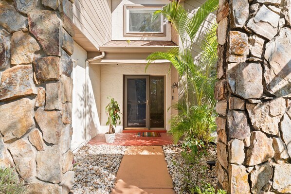 A house with a stone exterior, a front door, and a small garden area with plants and a pathway. - Tampa Oasis: Pool & Hot Tub Retreat for Families (Tampa)