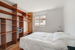 Une chambre à coucher avec un lit, des étagères en bois, une fenêtre et une table de chevet.