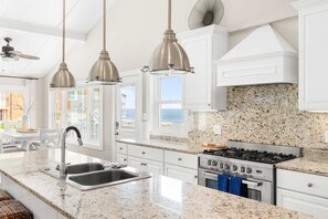 A kitchen with white cabinets, a granite countertop, stainless steel appliances, and pendant lighting. - Vagabond Penthouse | Ocean Views + Huge Deck (Ocean City)