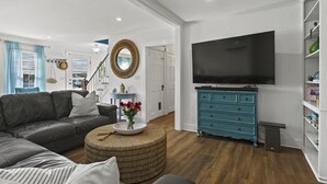 Uma sala de estar com sofá, mesa de centro, televisão e cômoda azul.