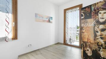 A room with a wooden floor, a painting on the wall, and a large mirror with a mask design.