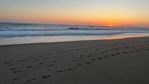 Een strand met voetafdrukken die naar het water leiden, golven en een zonsondergang.