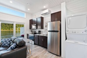 Eine moderne Küche mit Edelstahl-Kühlschrank, Mikrowelle und Herd, ein Essbereich mit Tisch und Stühlen sowie ein großes Fenster mit Blick auf ein Gewässer.