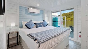 Un dormitorio con cama, mesita de noche, lámpara y vista a un cuerpo de agua a través de una puerta corredera.