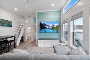 Una sala de estar moderna con un televisor de pantalla plana grande, una escalera y vistas a un lago.