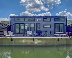 Un edificio moderno con un letrero que dice 'Welcome to the Lake' y un muelle con sillas y mesas.