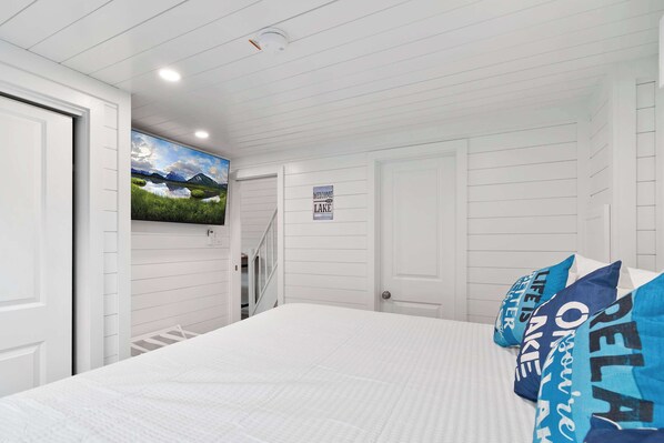 A bedroom with a bed, white walls, a welcome sign, a painting, and a staircase. - Summer Getaway Floating Home on Lake Cumberland (Russell Springs)