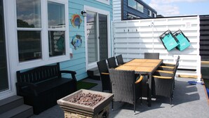 En terrasse med et træbord og stole, en sort bænk og en grill.