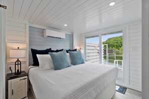 A bedroom with a bed, bedside table, lamp, and a view of a balcony. - Anchors Away - Floating House on Lake Cumberland (Russell Springs)