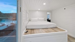 Een slaapkamer met een groot bed, een glazen deur naar een balkon en uitzicht op een waterpartij.