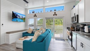 A modern kitchen with white cabinetry, a teal sofa, and a large window overlooking a lake. - Four Suns - Lake Front Floating House Retreat (Russell Springs)