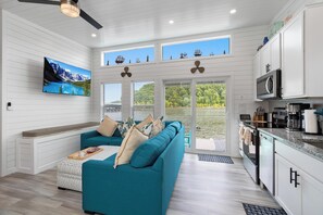 A modern kitchen with white cabinetry, a teal sofa, and a large window overlooking a lake. - Four Suns - Lake Front Floating House Retreat (Russell Springs)