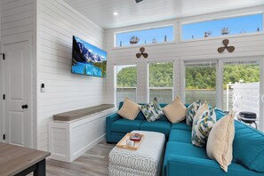 A modern living room with a teal sofa, a mounted TV, and a window overlooking a lush landscape. - Four Suns - Lake Front Floating House Retreat (Russell Springs)