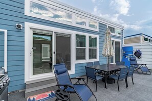 Une maison bleue dotée d’un patio comprenant une table, des chaises et un barbecue.