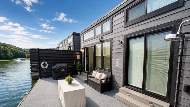 A modern building with large windows, a patio with outdoor furniture, and a view of a lake. - Pet-Friendly Floating House on the Lake (Russell Springs)