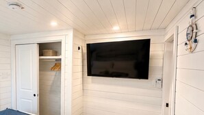 A bedroom with a bed, a TV mounted on the wall, a closet, and a small trash bin. - Pet-Friendly Floating House on the Lake (Russell Springs)