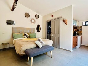 Ein Schlafzimmer mit Bett, Nachttisch, Bank und Blick zur Küche.