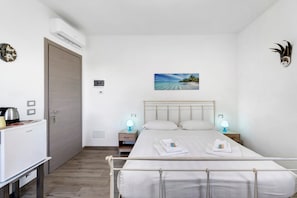 Une chambre à coucher avec un lit, des lampes de chevet, un tableau au mur, une porte et une petite table sur laquelle se trouve une bouilloire.