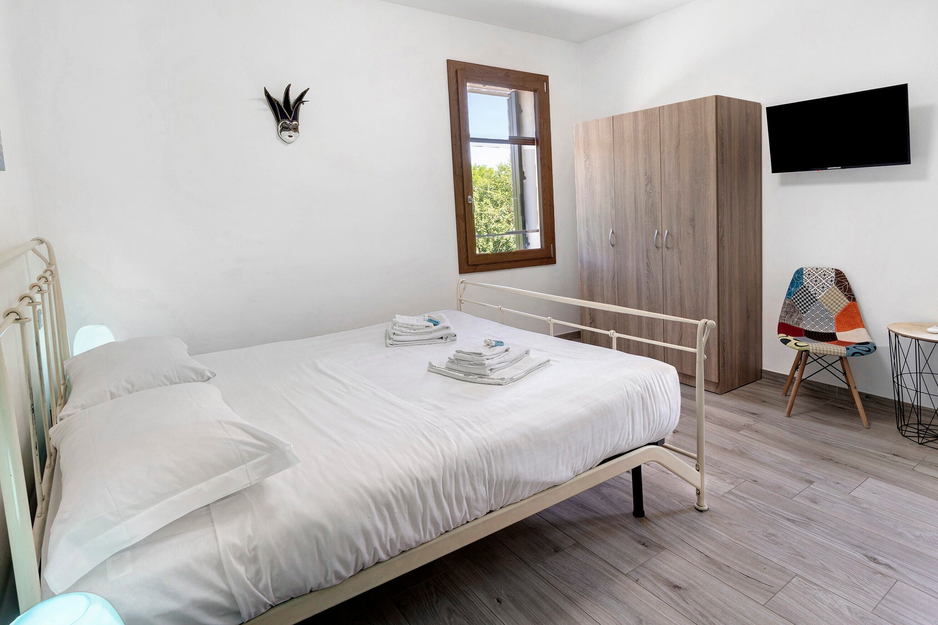 A bedroom with a bed, a wardrobe, a television, and a window.