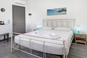 A neatly made bed with white linens and towels, a bedside table with a lamp, a small cabinet, and a picture of a beach on the wall. - Double Room with Wi-Fi and Air Conditioning (Mira)