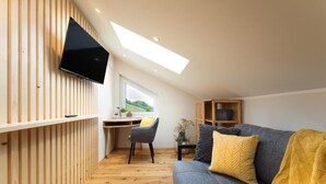 A modern loft bedroom with a skylight, a work desk, a gray sofa, and a small cabinet. - Das Weinkitz  (Kitzeck im Sausal)